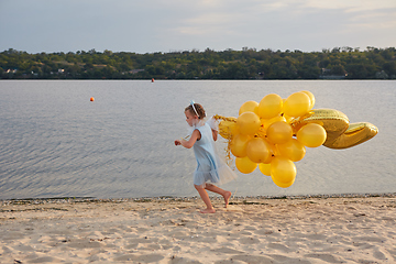 Image showing Little girl with many golden balloons on the beach at sunset