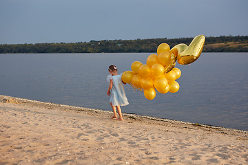 Image showing Little girl with many golden balloons on the beach at sunset