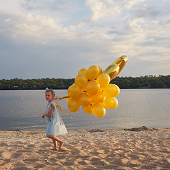 Image showing Little girl with many golden balloons on the beach at sunset