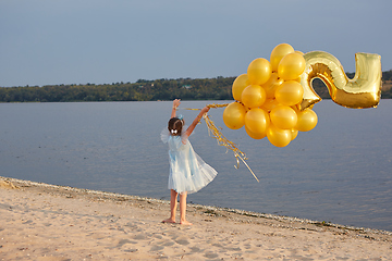 Image showing Little girl with many golden balloons on the beach at sunset