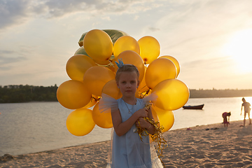 Image showing Little girl with many golden balloons on the beach at sunset