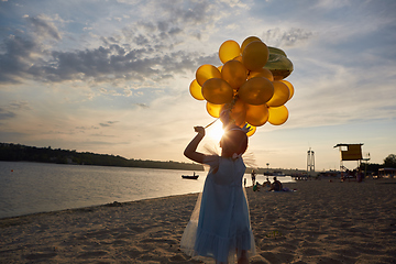 Image showing Little girl with many golden balloons on the beach at sunset