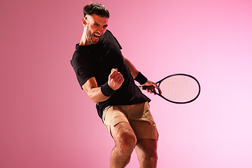 Image showing Young caucasian man playing tennis isolated on pink studio background, action and motion concept