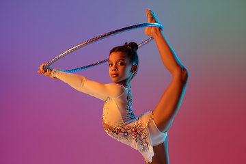 Image showing African-american rhythmic gymnast, pretty girl practicing on gradient studio background in neon light