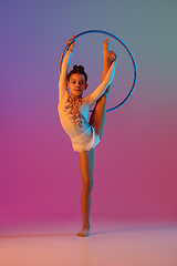 Image showing African-american rhythmic gymnast, pretty girl practicing on gradient studio background in neon light