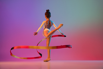 Image showing African-american rhythmic gymnast, pretty girl practicing on gradient studio background in neon light