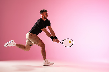 Image showing Young caucasian man playing tennis isolated on pink studio background, action and motion concept