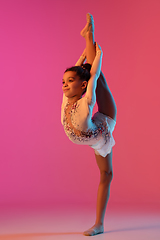 Image showing African-american rhythmic gymnast, pretty girl practicing on gradient studio background in neon light