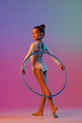 Image showing African-american rhythmic gymnast, pretty girl practicing on gradient studio background in neon light