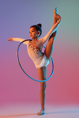 Image showing African-american rhythmic gymnast, pretty girl practicing on gradient studio background in neon light