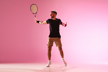 Image showing Young caucasian man playing tennis isolated on pink studio background, action and motion concept