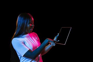 Image showing African young woman\'s portrait on dark studio background in neon. Concept of human emotions, facial expression, youth, sales, ad.