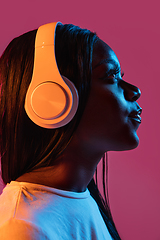 Image showing African young woman\'s portrait on pink studio background in neon. Concept of human emotions, facial expression, youth, sales, ad.