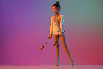 Image showing African-american rhythmic gymnast, pretty girl practicing on gradient studio background in neon light