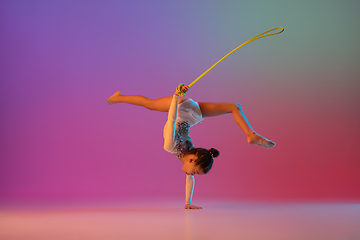 Image showing African-american rhythmic gymnast, pretty girl practicing on gradient studio background in neon light