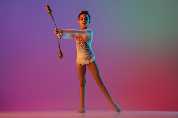 Image showing African-american rhythmic gymnast, pretty girl practicing on gradient studio background in neon light