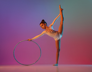 Image showing African-american rhythmic gymnast, pretty girl practicing on gradient studio background in neon light