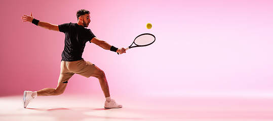 Image showing Young caucasian man playing tennis isolated on pink studio background, action and motion concept