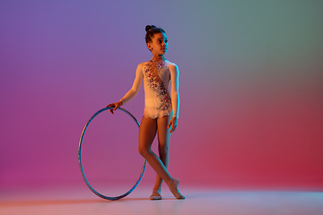 Image showing African-american rhythmic gymnast, pretty girl practicing on gradient studio background in neon light