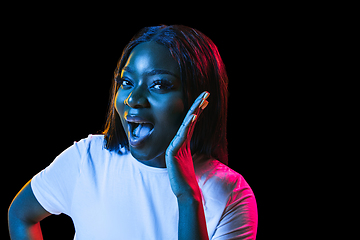Image showing African young woman\'s portrait on dark studio background in neon. Concept of human emotions, facial expression, youth, sales, ad.