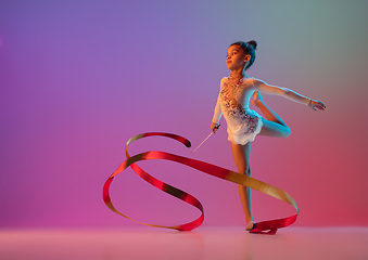 Image showing African-american rhythmic gymnast, pretty girl practicing on gradient studio background in neon light