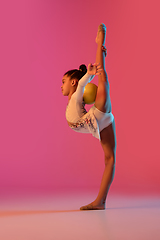 Image showing African-american rhythmic gymnast, pretty girl practicing on gradient studio background in neon light