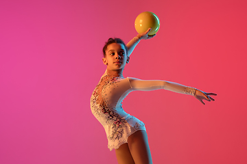 Image showing African-american rhythmic gymnast, pretty girl practicing on gradient studio background in neon light