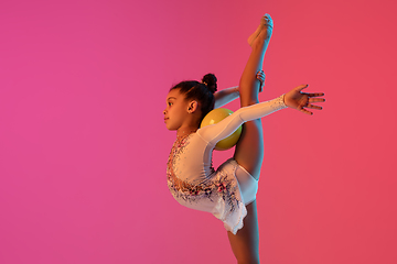 Image showing African-american rhythmic gymnast, pretty girl practicing on gradient studio background in neon light