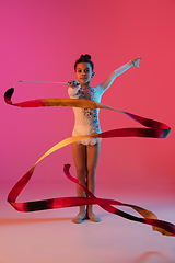 Image showing African-american rhythmic gymnast, pretty girl practicing on gradient studio background in neon light