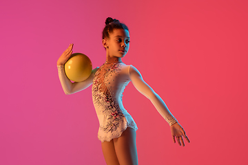 Image showing African-american rhythmic gymnast, pretty girl practicing on gradient studio background in neon light