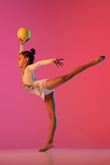 Image showing African-american rhythmic gymnast, pretty girl practicing on gradient studio background in neon light