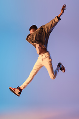 Image showing Young stylish man in modern street style outfit isolated on gradient background in neon light. African-american fashionable model in look book, musician performing.