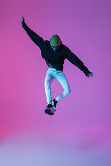 Image showing Young stylish man in modern street style outfit isolated on gradient background in neon light. African-american fashionable model in look book, musician performing.