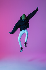 Image showing Young stylish man in modern street style outfit isolated on gradient background in neon light. African-american fashionable model in look book, musician performing.