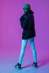 Image showing Young stylish man in modern street style outfit isolated on gradient background in neon light. African-american fashionable model in look book, musician performing.