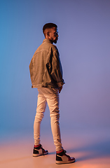 Image showing Young stylish man in modern street style outfit isolated on gradient background in neon light. African-american fashionable model in look book, musician performing.