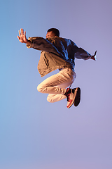 Image showing Young stylish man in modern street style outfit isolated on gradient background in neon light. African-american fashionable model in look book, musician performing.