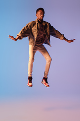 Image showing Young stylish man in modern street style outfit isolated on gradient background in neon light. African-american fashionable model in look book, musician performing.