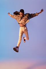 Image showing Young stylish man in modern street style outfit isolated on gradient background in neon light. African-american fashionable model in look book, musician performing.