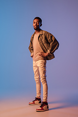 Image showing Young stylish man in modern street style outfit isolated on gradient background in neon light. African-american fashionable model in look book, musician performing.