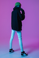 Image showing Young stylish man in modern street style outfit isolated on gradient background in neon light. African-american fashionable model in look book, musician performing.