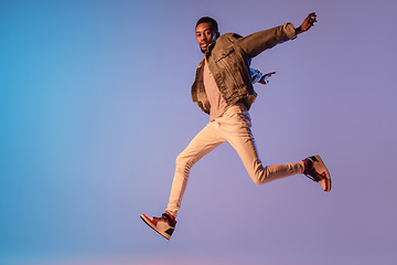 Image showing Young stylish man in modern street style outfit isolated on gradient background in neon light. African-american fashionable model in look book, musician performing.