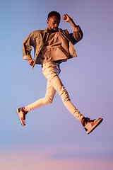 Image showing Young stylish man in modern street style outfit isolated on gradient background in neon light. African-american fashionable model in look book, musician performing.