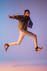 Image showing Young stylish man in modern street style outfit isolated on gradient background in neon light. African-american fashionable model in look book, musician performing.