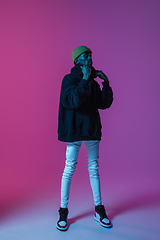 Image showing Young stylish man in modern street style outfit isolated on gradient background in neon light. African-american fashionable model in look book, musician performing.