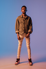 Image showing Young stylish man in modern street style outfit isolated on gradient background in neon light. African-american fashionable model in look book, musician performing.