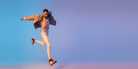 Image showing Young stylish man in modern street style outfit isolated on gradient background in neon light. African-american fashionable model in look book, musician performing.