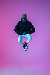 Image showing Young stylish man in modern street style outfit isolated on gradient background in neon light. African-american fashionable model in look book, musician performing.