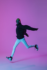 Image showing Young stylish man in modern street style outfit isolated on gradient background in neon light. African-american fashionable model in look book, musician performing.