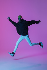 Image showing Young stylish man in modern street style outfit isolated on gradient background in neon light. African-american fashionable model in look book, musician performing.